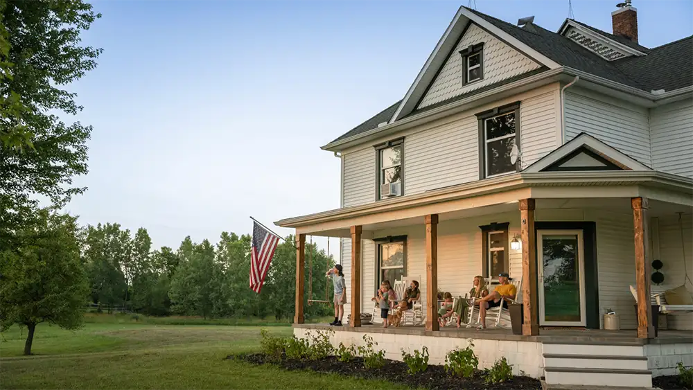 A multi-generational family relaxes on the expansive porch of a beautifully maintained Michigan farmhouse with a new architectural shingle roof, representing the peace of mind and structural protection provided by MI Roof Pro.